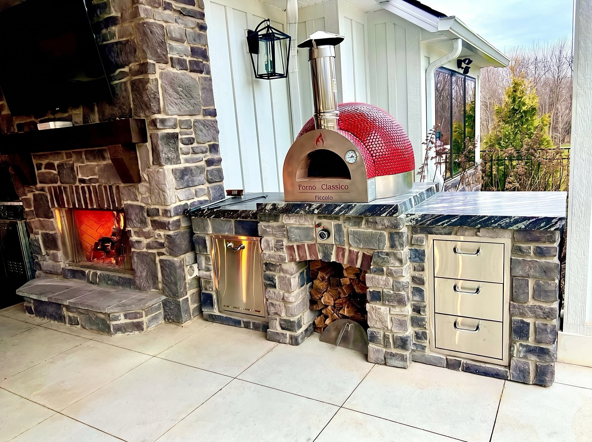 Outdoor kitchen with stone fireplace and Forno Classico Piccolo 65 pizza oven on a patio