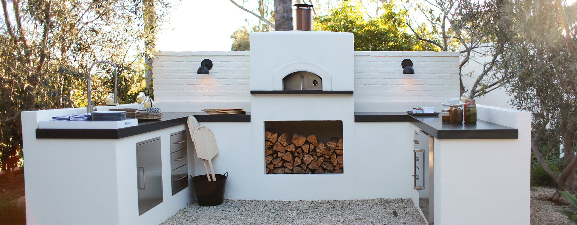 Forno Classico Fiamma with white cabinets, black countertops, and a wood-fired oven in an outdoor setting.