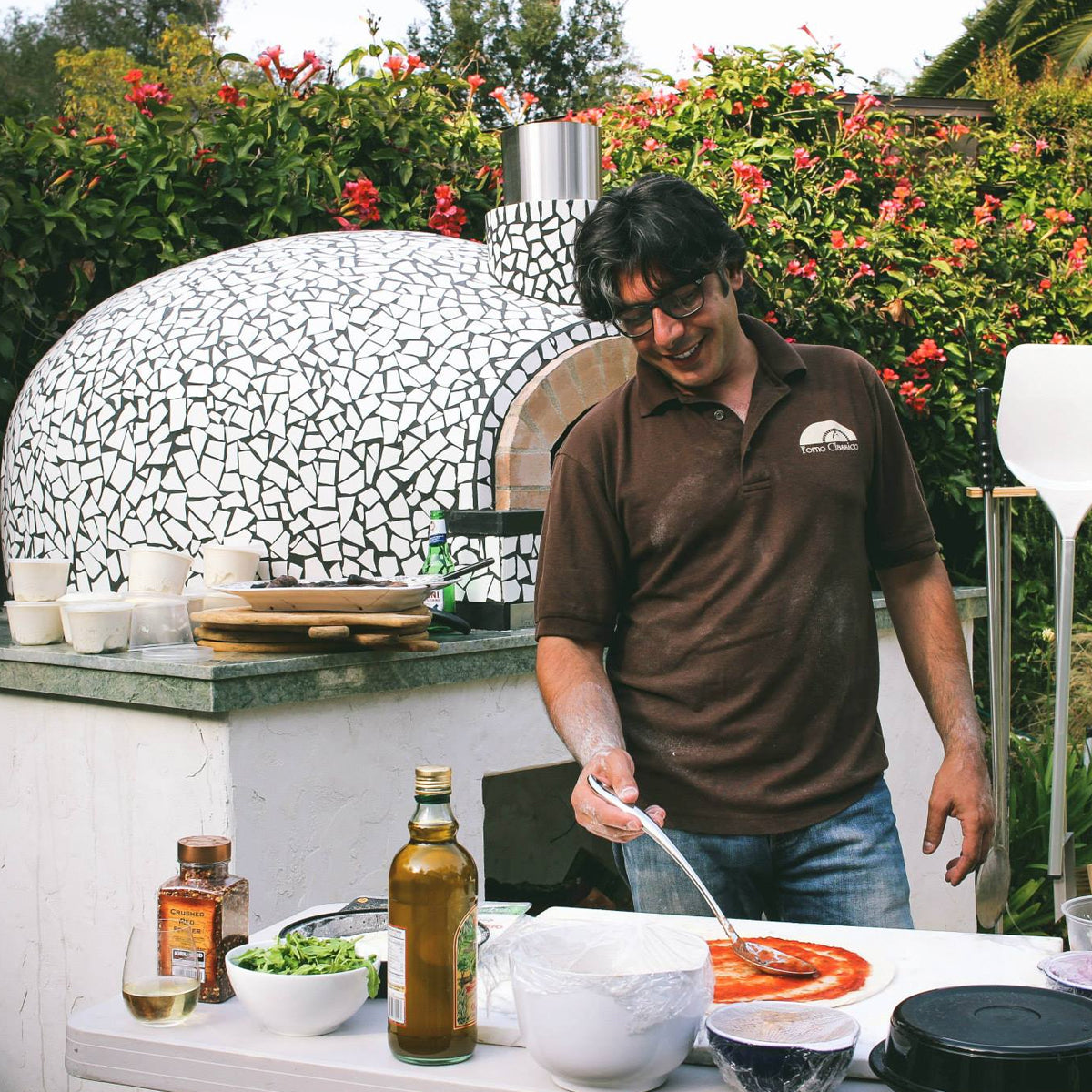 Giuseppe Crisa, preparing food outdoors with a Forno Classico pizza oven in the background.
