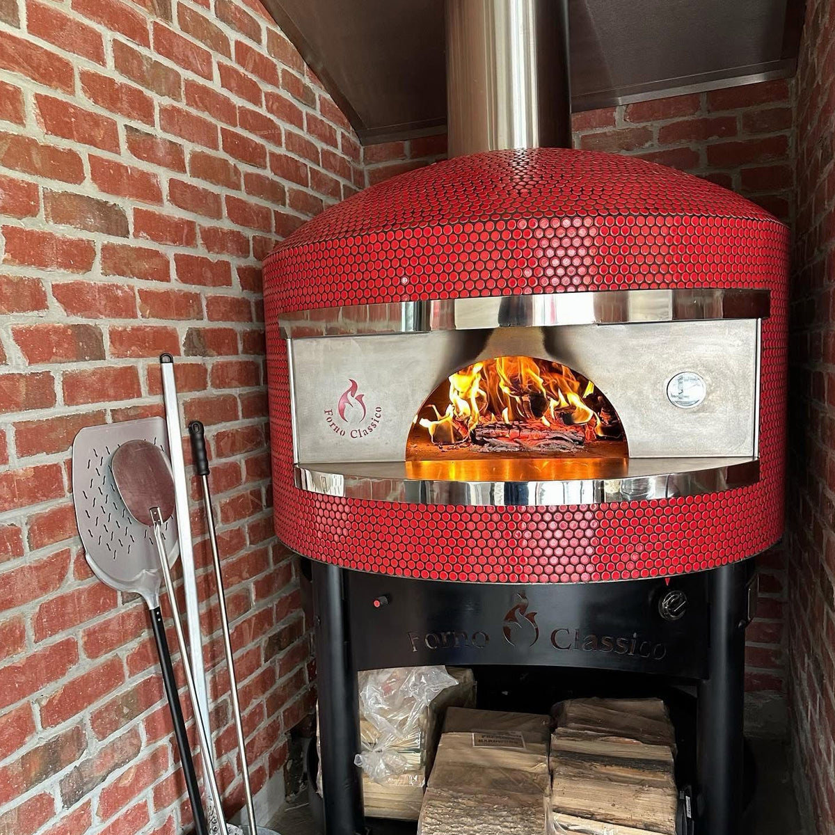 Forno Classico outdoor pizza oven with flames inside, mounted on a brick wall.