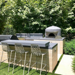 Outdoor kitchen with Forno Classico pizza oven and bar stools in a garden setting