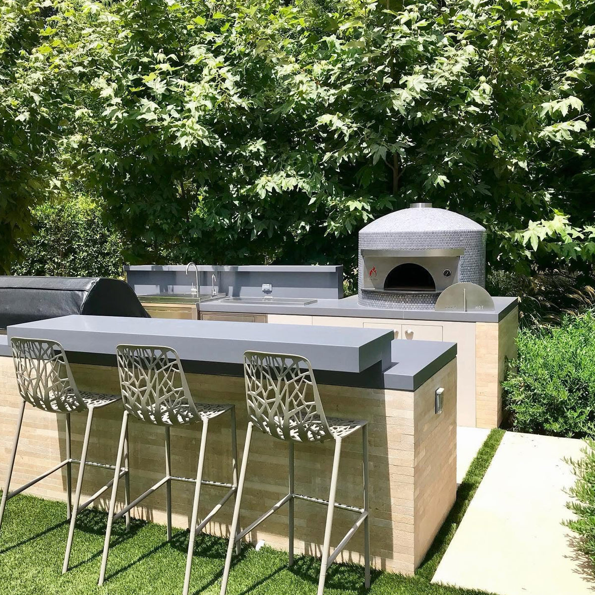 Outdoor kitchen with Forno Classico pizza oven and bar stools in a garden setting