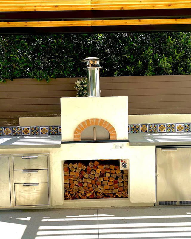 Forno Classico Fiamma Square in an outdoor kitchen with fire wood beneath it.